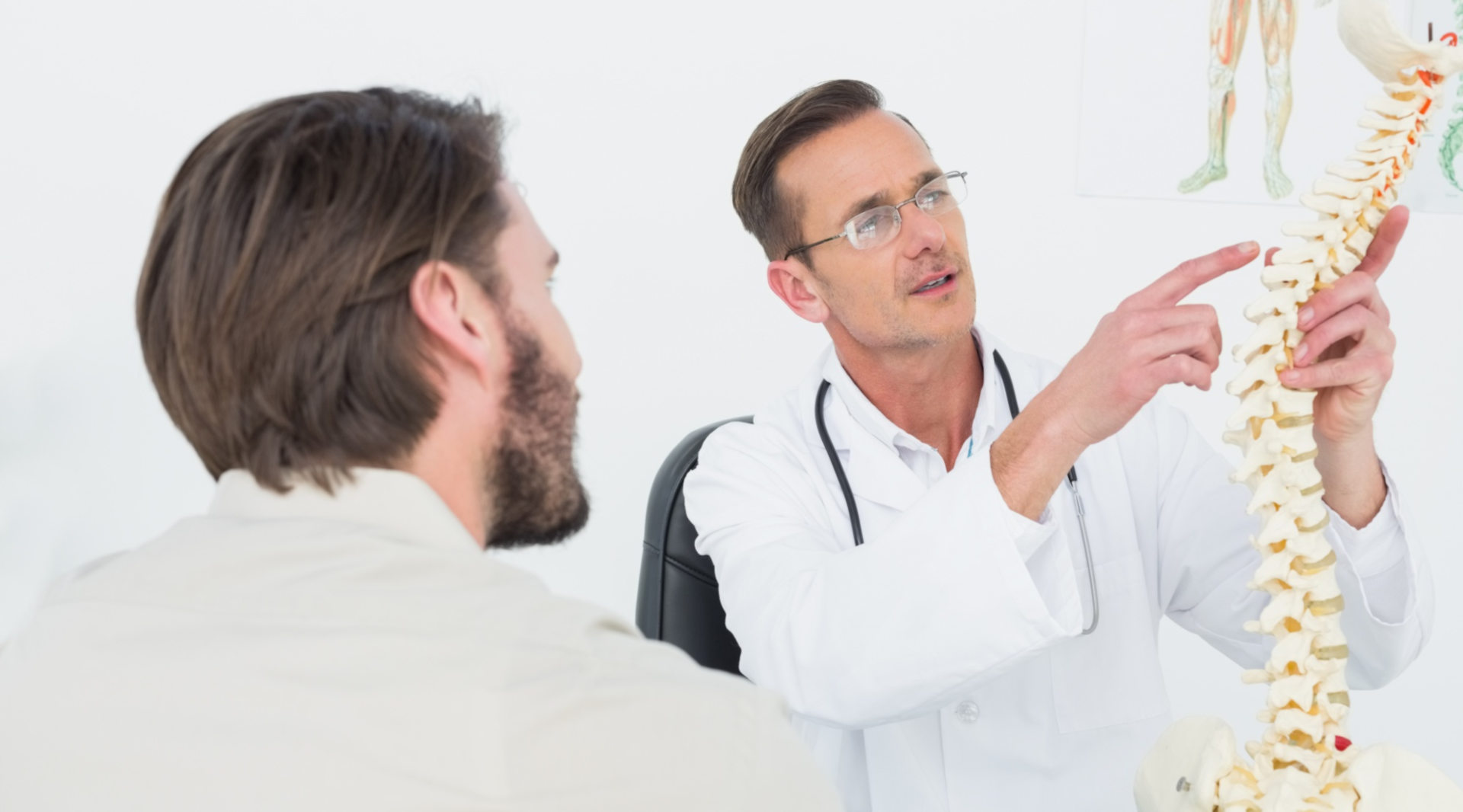 Arzt klärt Patienten an einem Wirbelsäulen-Modell über geplante OP auf
